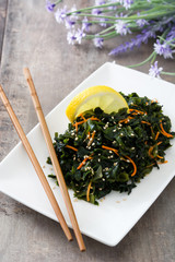 Wakame salad with carrot, sesame seeds and lemon juice in plate on wooden table
