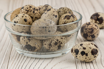 Quail eggs in a glass bowl on old white wooden table.