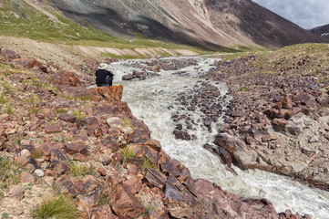 a man sitting on a rock in the mountain river, looking into the