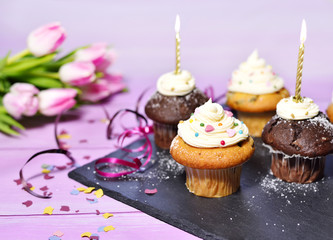 Delicious cupcakes with icing and confetti decoration. Birthday scene with tulip bouquet and burning candles.