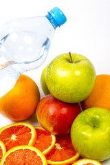 Concept of healthy lifestyle. Green and red apples, orange. Sliced red orange. Bottle of pure drinking water in background. Close up image. Vitamins and healthy nutrition for fitness.