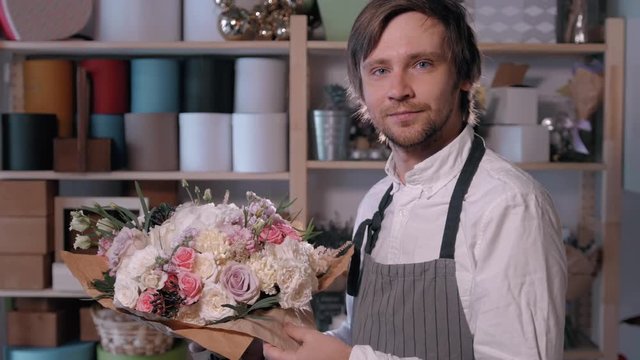 happy smiling florist man making fashion bunch at flower shop. people, business, sale and floristry concept. Bouquet with roses, peone, lilac and lisianthus