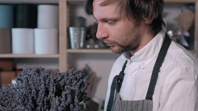 happy smiling florist man making bunch at flower shop. people, business, sale and floristry concept. Bouquet with lavender