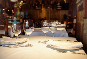 Empty glasses in a restaurant on white tablecloth. Shade, brown background and carved chairs.