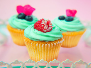 Cupcakes with butter cream and vanilla with raspberry and blueberry with pink flowers on the tray on pink background