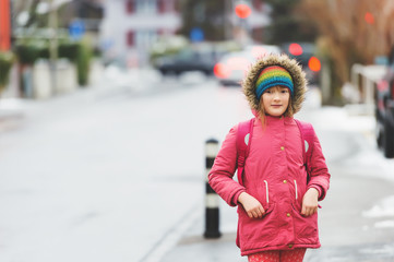 Little schoolgirl with backpack in winter, wearing warm red jacket