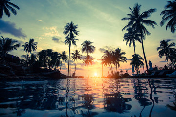 Fototapeta na wymiar Tropical beach with pool and silhouetted palm trees during sunset.