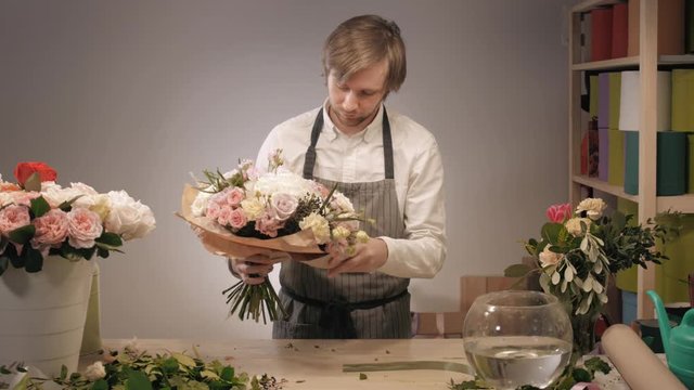 Photo of smiling florist standing with a colorful bouquet in flower shop. Bouquet with roses, peone, lilac and lisianthus