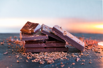 Dark chocolate pieces stacked on slate plate against background with reflections of light. Copy space. Closeup. Selective color.