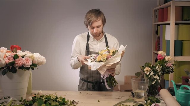 Photo of smiling florist standing with a colorful bouquet in flower shop. Bouquet with roses, peone, lilac and lisianthus