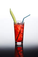 Cocktail with red tonic, grenadine and vodka in tall glass with fresh cucumber slice, ice and blue straw. On reflective background.