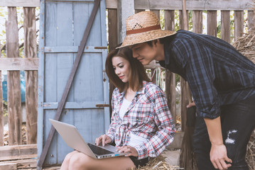 Farming couple with laptop,smartphone in hay shed.