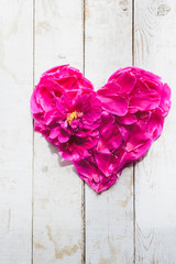 Fototapeta premium top view of red peonies petals in heart shape as love symbol for wedding or valentines day decorate on wooden board background