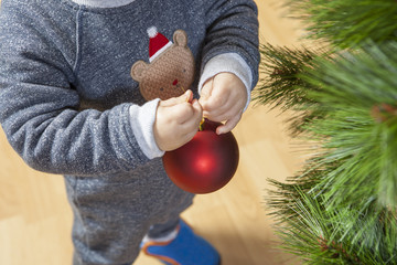 Baby boy decorates Xmas Tree with red ball