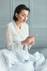 Woman in the bed reading a message on your phone.