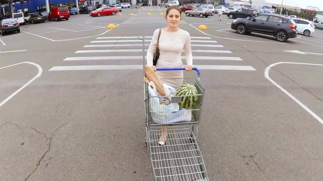 Beautiful young woman walking with full shopping cart from the supermarket