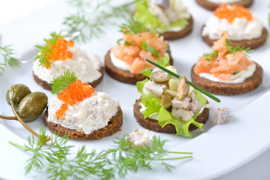 Leckeres Fisch-Fingerfood mit Lachstatar, Matjestatar und Forellencreme mit Kaviar -  Finger food with salmon tartar, trout mousse with caviar and herring salad on pumpernickel bread 