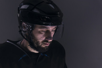 Naklejka premium EXTREME CU Portrait of Caucasian male ice hockey player in dark uniform, black helmet, dramatic lighting