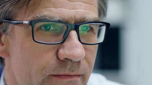Close-up of a Male Senior Doctor Working at His Desk on a Personal Computer. Reflection of the Screen Seen in His Glasses. Shot on RED Cinema Camera 4K (UHD).