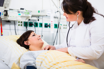 Ärztin auf Intensivstation eines Krankenhauses hört ihre Patientin mit einem Stethoskop ab