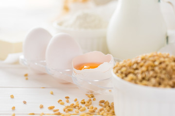 Ingredients for baking: flour, milk, wheat grain, butter and eggs on white wooden background. Selective focus
