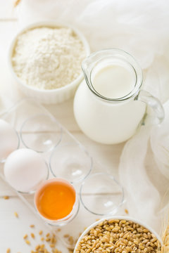 Ingredients for baking: flour, milk, wheat grain, butter and eggs on white wooden background. Selective focus
