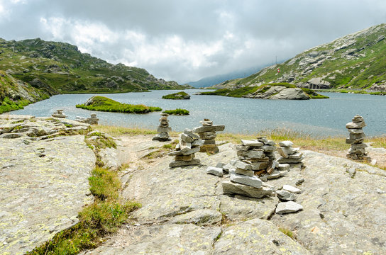 Rock piles on slab in the Swiss Alps with a mountain lake behind that extends to the horizon. A Swiss flag is seen on a little island in the middle of the lake
