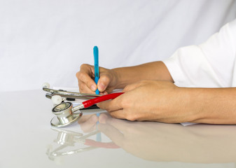 Doctor holding stethoscope and writing treat report on clipboard