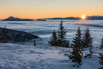 First sunrays on mountains above low clouds