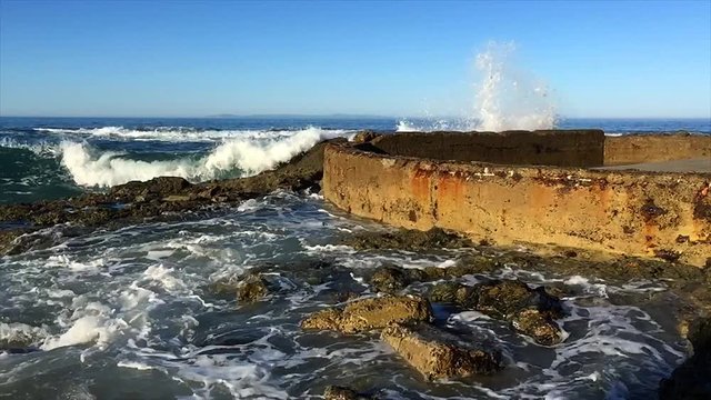 Slow motion waves along a rocky beach and seawall crash and swirl over the shallow reef system during a morning sunrise.