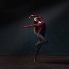 Young woman ballet dancer near dark blue grunge wall background