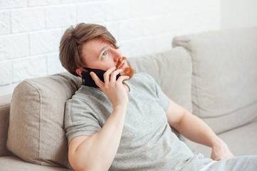 The bearded man sitting on the couch at home and calling the phone