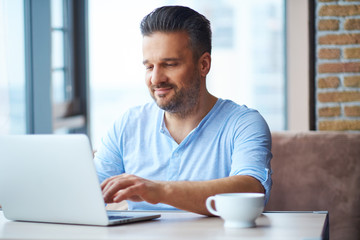 Fototapeta premium Handsome man with cup of coffee using laptop at home
