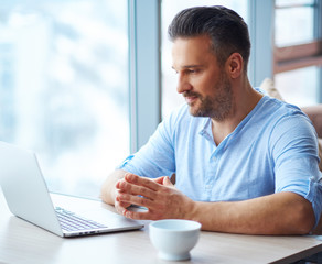 Handsome man with cup of coffee using laptop at home