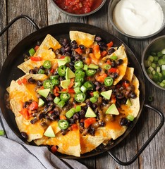 Classic Nachos with Tortilla chips melted cheese sauce jalapeno peppers avocado salsa and sour cream / Game day food