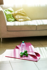 Fitness tools with mineral water on yoga mat in the room
