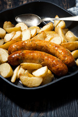 fried pork sausages with potatoes in frying pan, closeup 