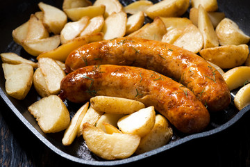 fried pork sausages with potatoes in frying pan, closeup