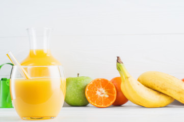A glass of fresh orange juice and fruits, orange, tangerine, apple, banana on white wooden background with copy space. Healthy lifestyle  and diet concept. Healthy eating for weight loss.