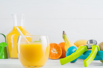 A glass of fresh orange juice and fruits, tangerine, apple, banana, dumbbell, hand gripper on white wooden background. Healthy lifestyle and diet concept. Healthy eating for weight loss. 