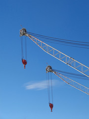 Boom lifting cranes in port against blue sky