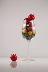 Wineglass filled with fresh small vegetables on a white background. One small tomatoe nex to a glass