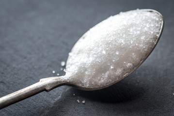 Spoon with white sugar on the dark background