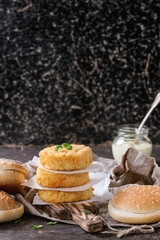 Ingredients for making vegan burger. Veggie cheese and onion cutlets, yogurt sauce, hamburger bunsand  herbs , served on wooden board with textile on dark background. Healthy vegan food.