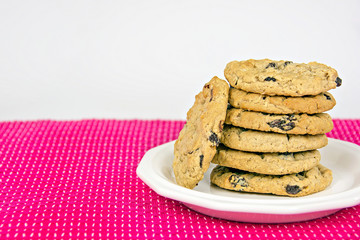 oatmeal cookies with raisins stacked on white plate with bright pink tablecloth