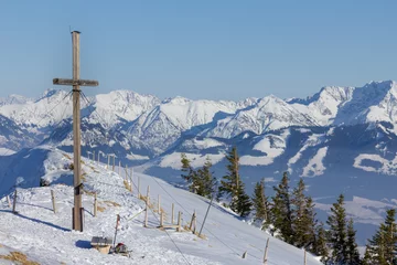 Fotobehang Summit cross in winter with outlook to a mountain range. © Drepicter