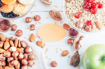 Healthy food. Ingredients for healthy breakfast on white wooden background with blank sticker. Oatmeal, dried cherry, apricots, figs and nuts, close up, top view. The concept of natural organic food.