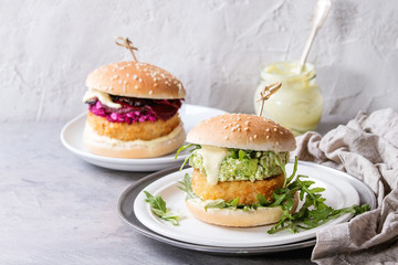 Two vegetarian hamburgers with onion and cheese cutlets, avocado salad, arugula, fried beetroot and yogurt sauce in white plate over gray texture background. Healthy fast food.