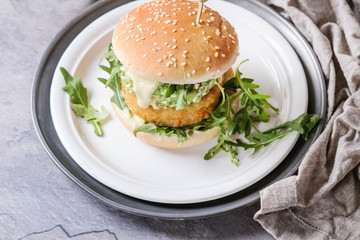 Vegetarian hamburger with onion and cheese cutlets, avocado salad, arugula and yogurt sauce in white plate over gray texture background. Healthy fast food. Close up