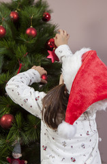 Little girl decorates Xmas Tree with red ball